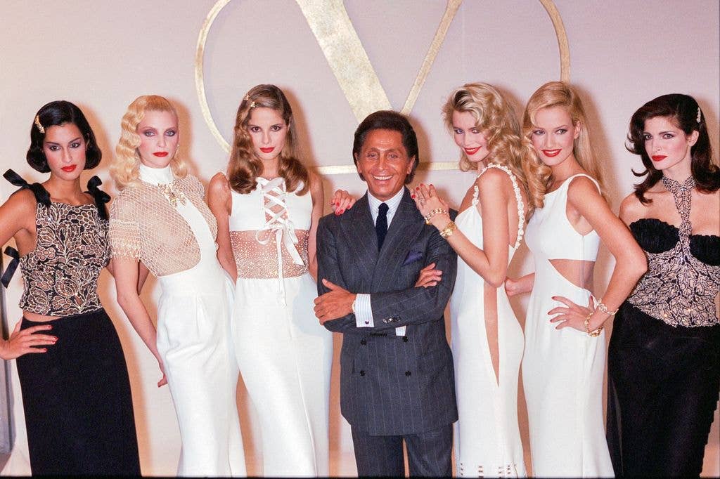 Valentino pose backstage with, Claudia Schiffer, Karen Mulder and Stephanie Seymour who are wearing white dresses. Valentino wears a grey suit with shirt and tie
