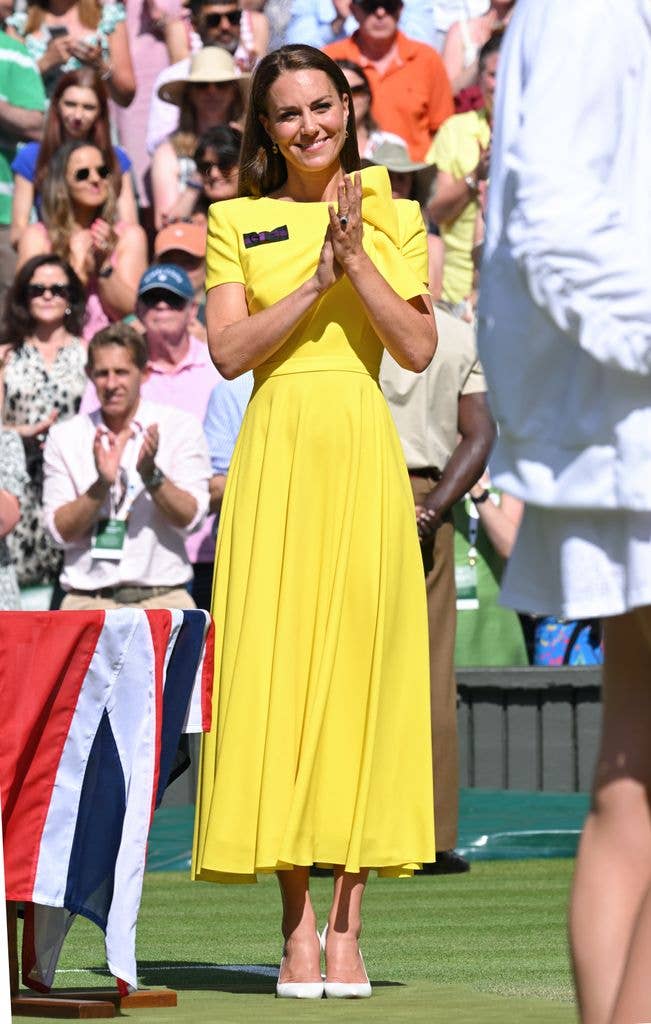 Kate Middleton at Wimbledon, 2022 clapping on the lawn, wearing a bright yellow dress and red heels