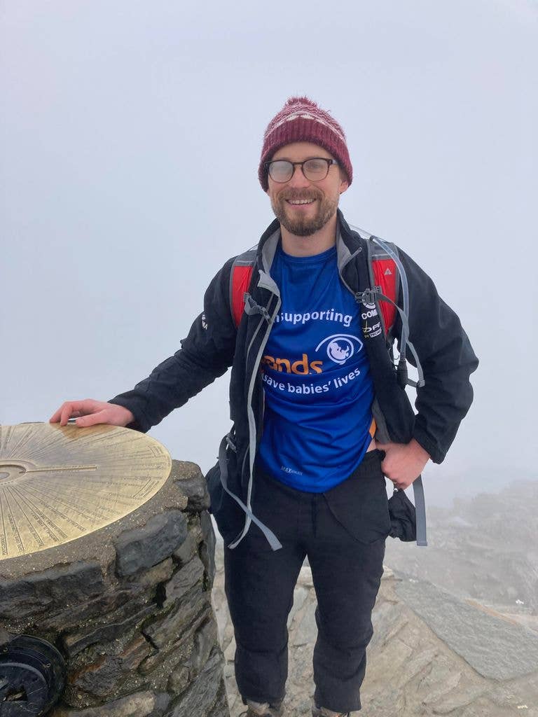 Man in hiking gear with hand on trig point in the mist
