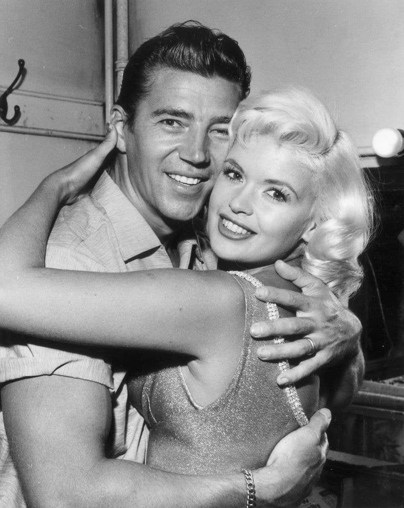 Jayne Mansfield and her husband, Mickey Hargitay hug one another and look at the camera.