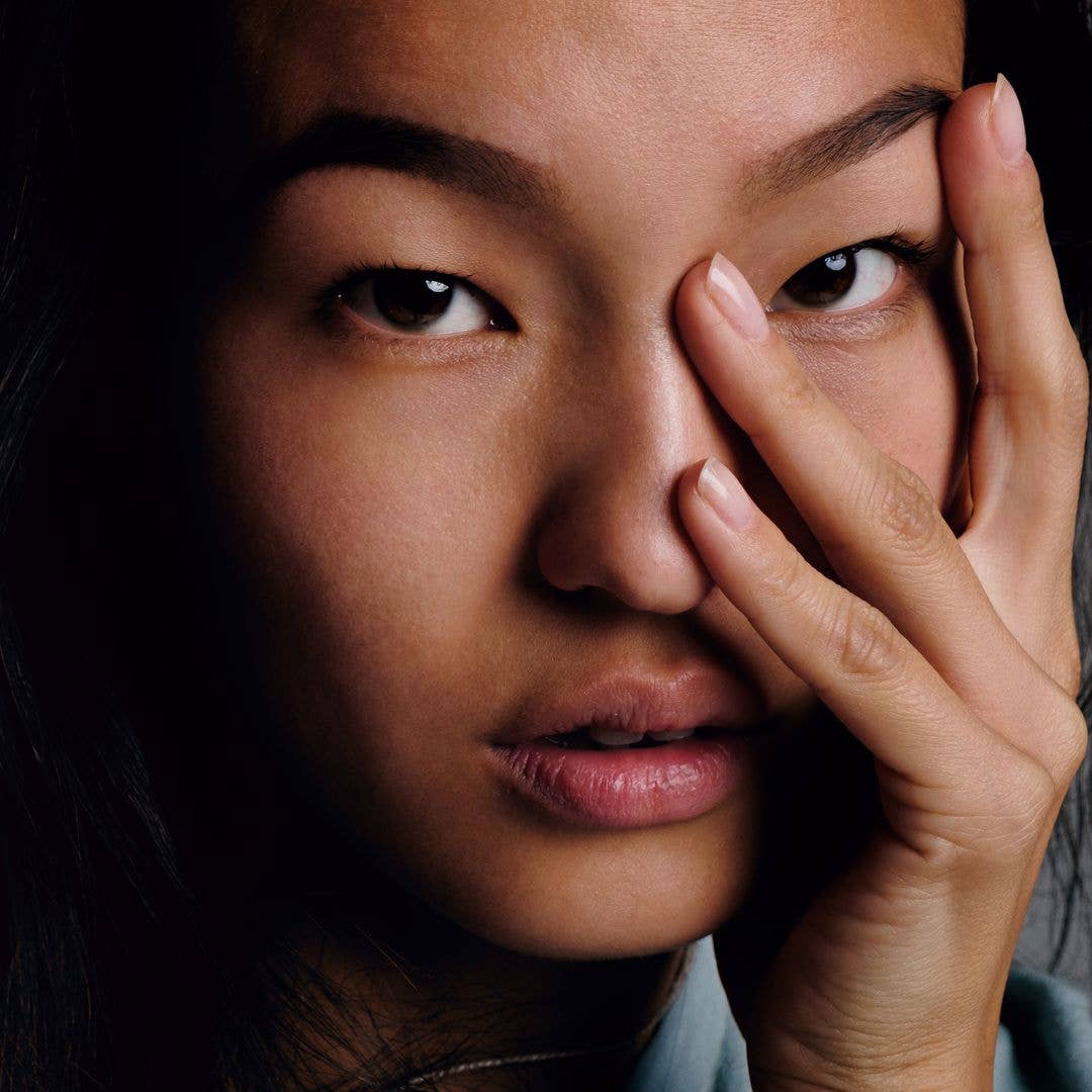 Close-up of calm Korean girl with smooth skin looking at camera with fingers on face