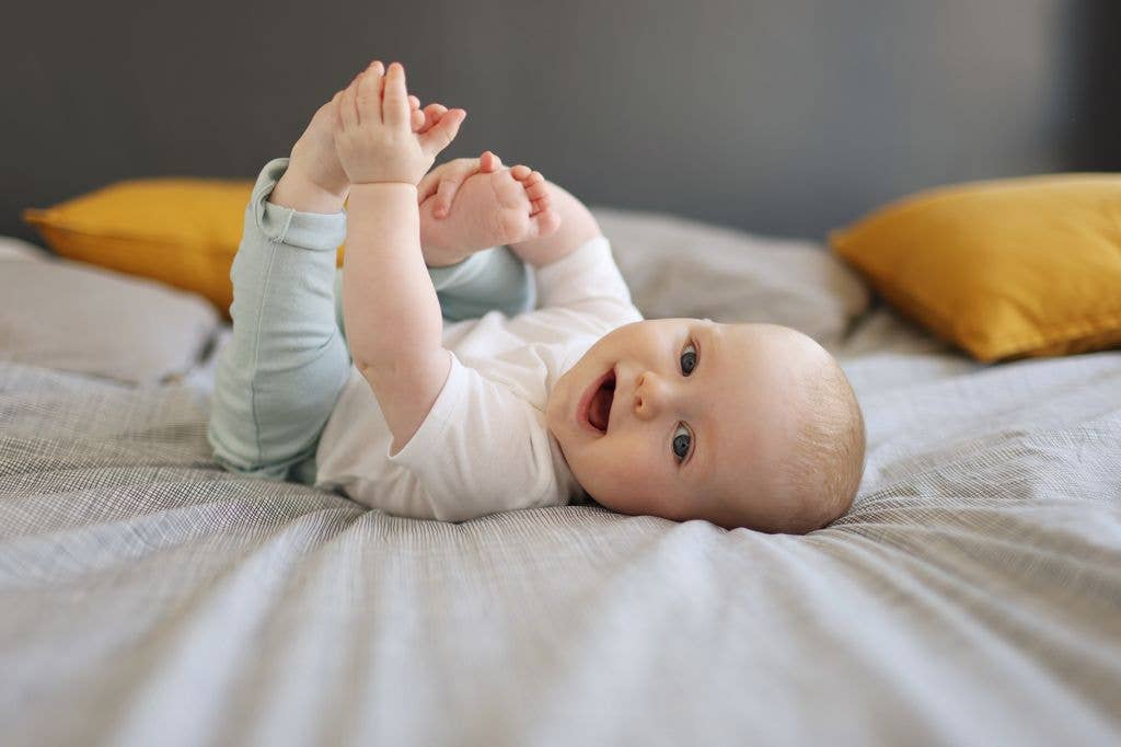 Portrait of a smiling baby at home, he's holding his foot