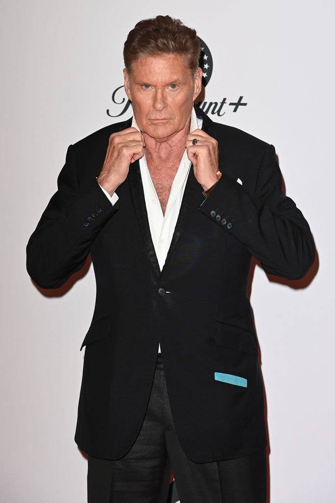 David Hasselhoff in a black suit and white shirt fixes his collar.