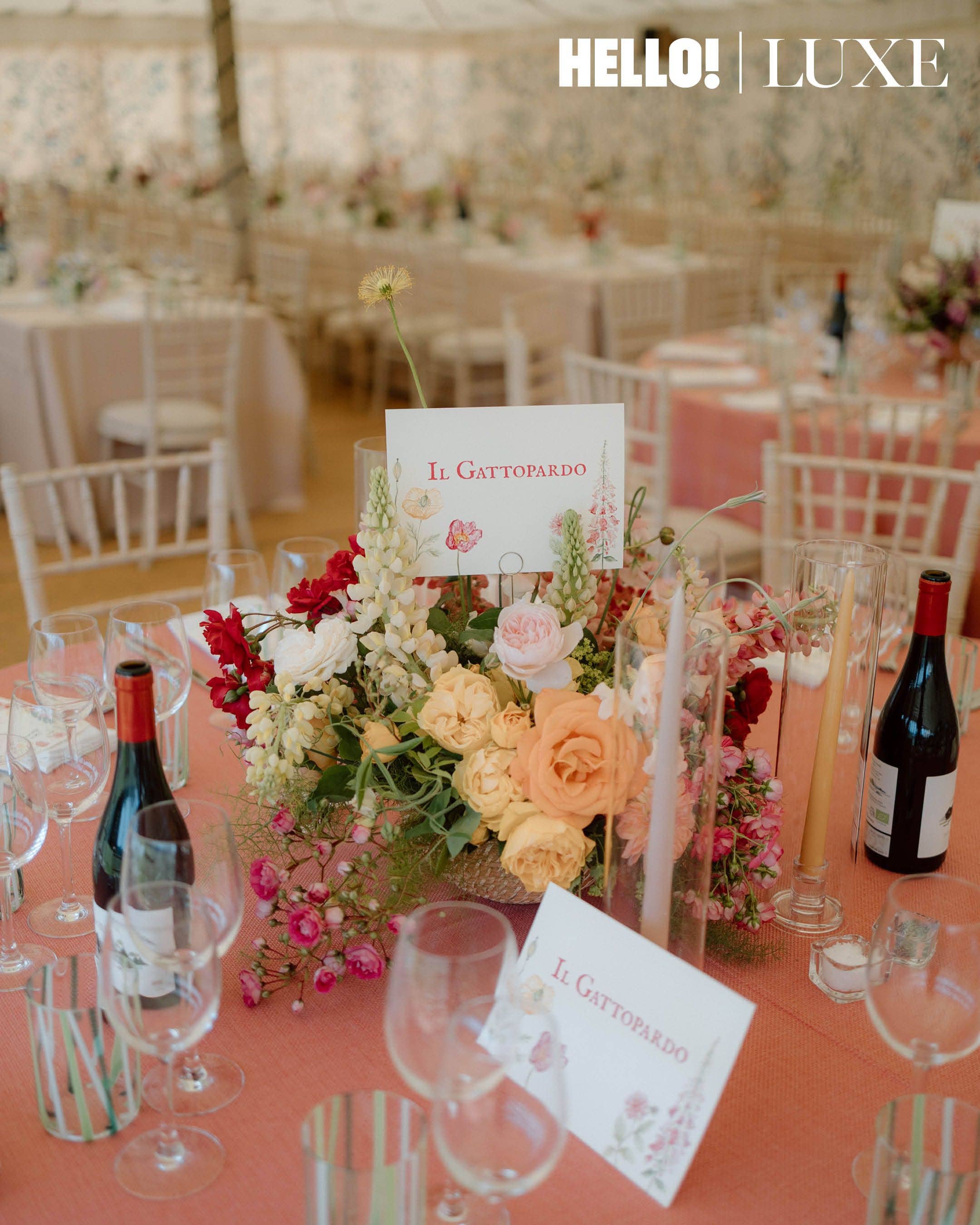One of the round tables inside the marquee, decorated with peach and cream roses, foxgloves, and a centerpiece card for the film Il Gattopardo