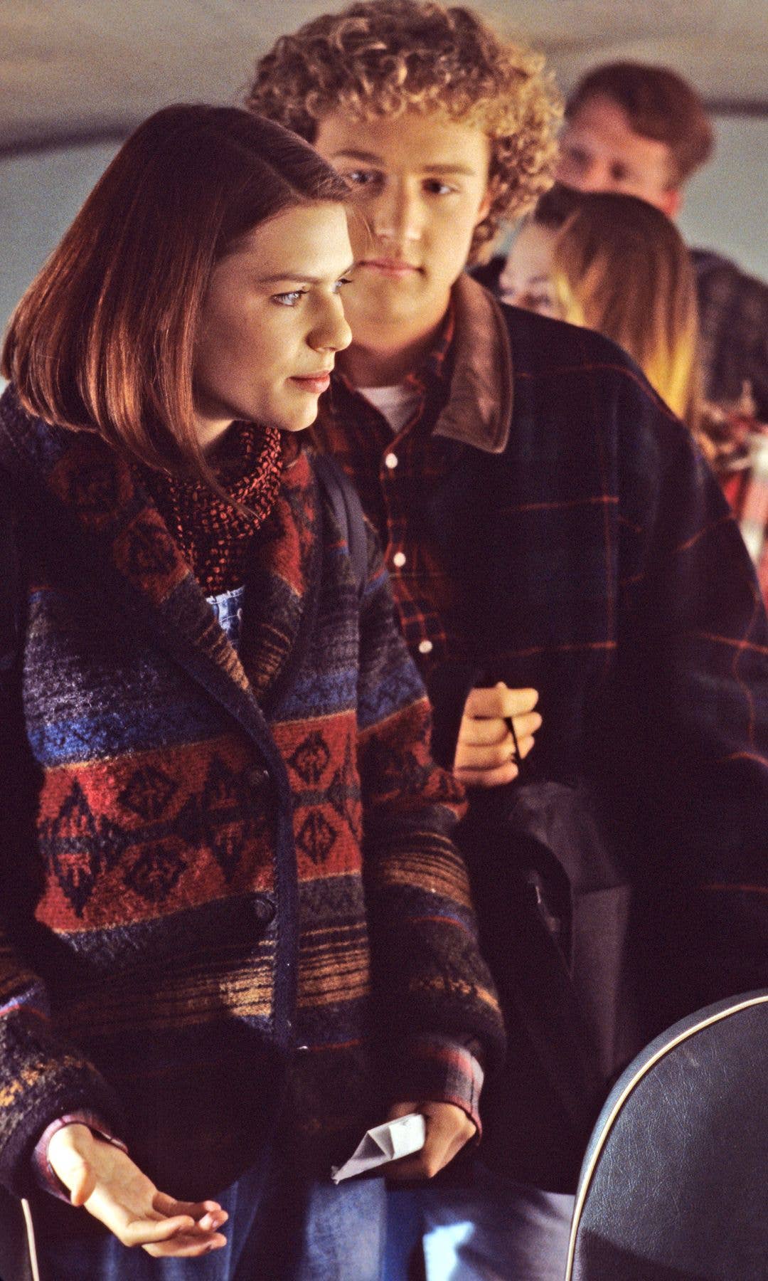 Claire Danes stands next to a man with curly hair, both looking ahead in a bus.