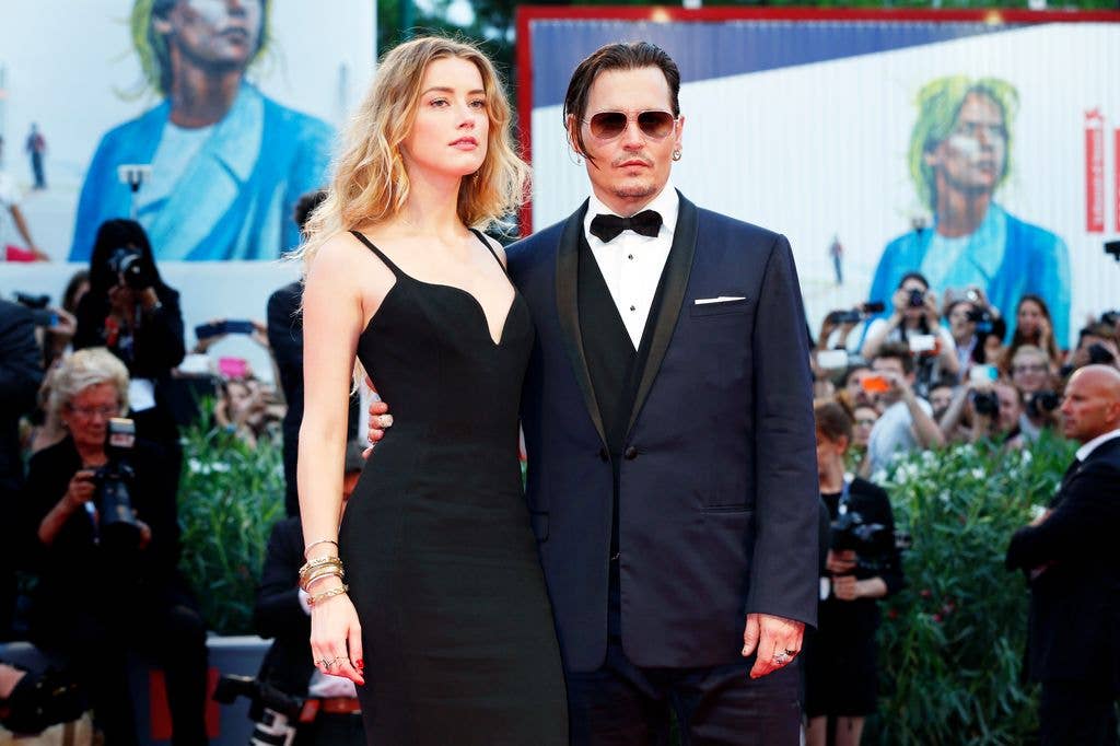 Johnny Depp and Amber Heard posing for photos on a red carpet, he is wearing sunglasses