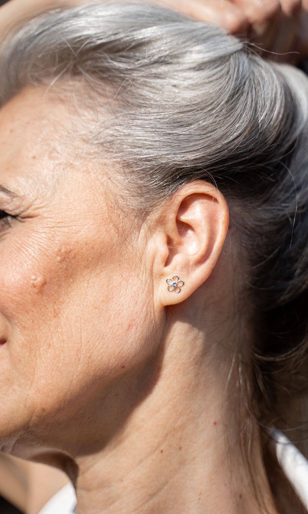 Older woman with grey hair holding it up in a bun