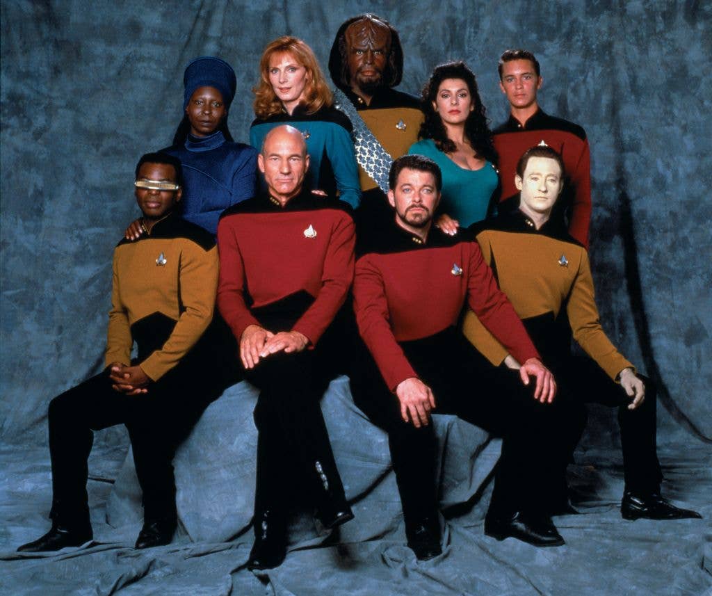 Star Trek: The Next Generation cast in 1987. Pictured are from left, front row, American actor LeVar Burton (as Lieutenant Commander Geordi La Forge), British actor Patrick Stewart (as Captain Jean-Luc Picard), and American actors Jonathan Frakes (as Commander William T. Riker) and Brent Spiner (as Lieutenant Commander Data); from left, back row, American actors Whoopi Goldberg (as Guinan), Gates McFadden (as Doctor Beverly Crusher), and Michael Dorn (as Lieutenant Worf), British-American actress Marina Sirtis (as Counselor Deanna Troi), and American actor Wil Wheaton (as Wesley Crusher). 