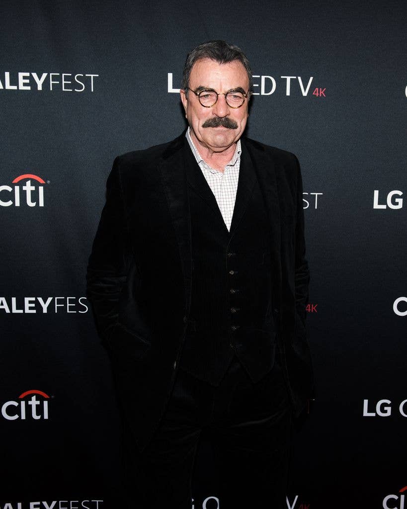 Tom Selleck in a black suit with a pale blue checked shirt.