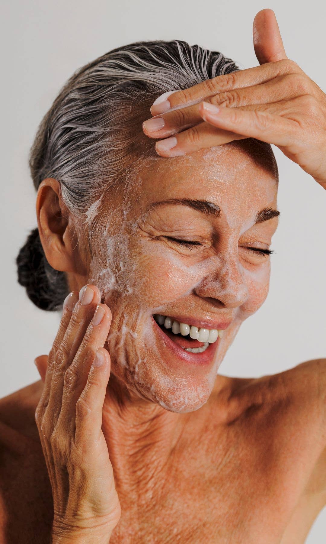 Mature model with her hair in a grey bun cleansing her face