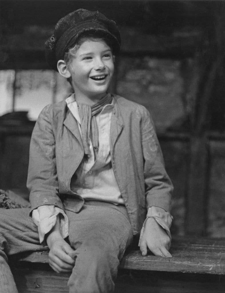 Mark Lester sitting on a step in a cap and tattered outfit as Oliver in the musical Oliver!