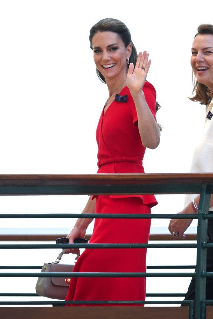 Kate Middleton waves while wearing a red dress and holding a handbag.