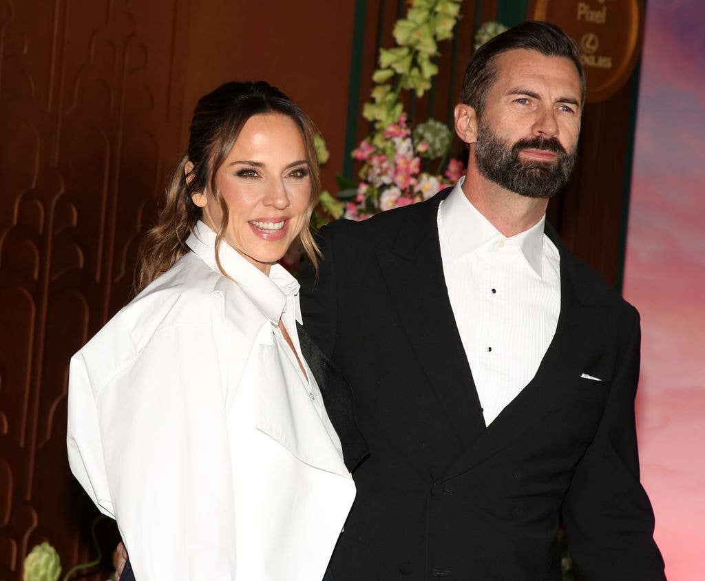 Melanie C and Scott Dingwall in formal attire stand close together, smiling.