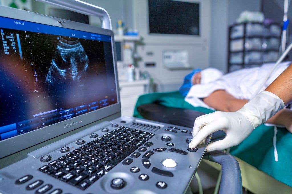 Person in gloves operates ultrasound machine in a hospital room.