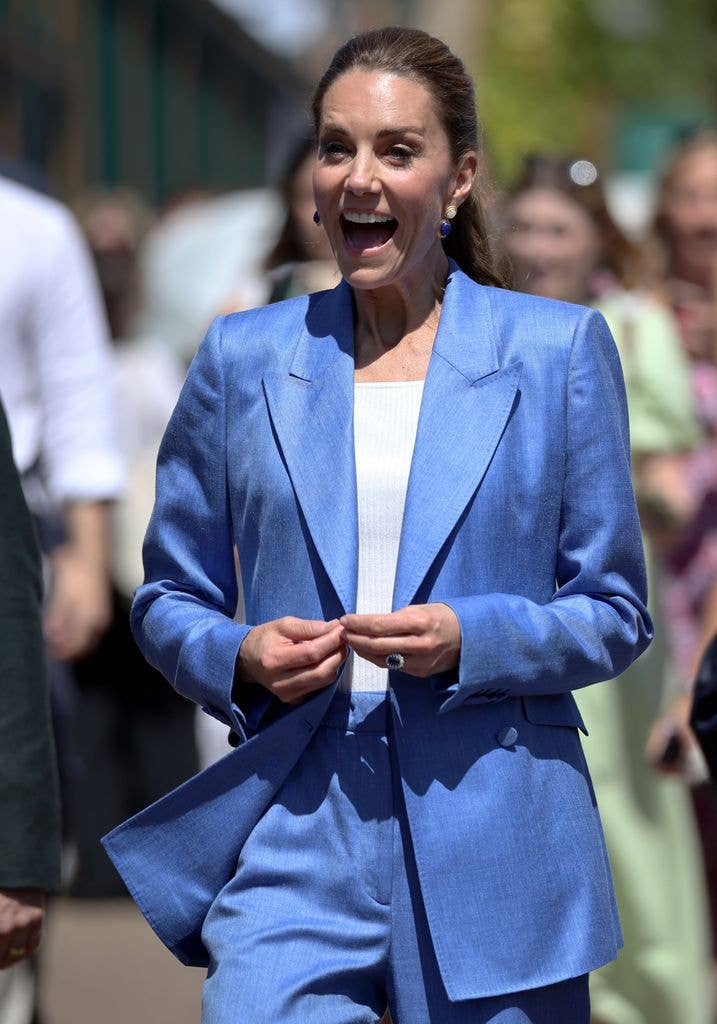 Kate Middleton, wearing a blue suit, smiles and walks among a crowd.