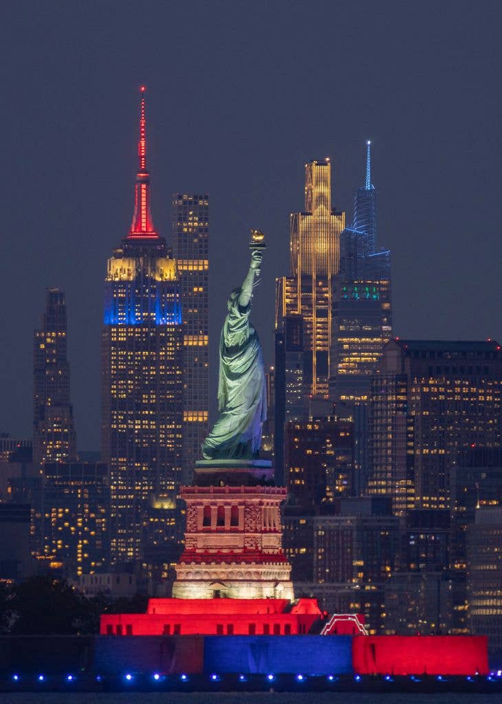 The Empire State Building is illuminated in the colors of the flag of France to mark their FIFA World Cup 2026 victory over Sweden, behind the Statue of Liberty illuminated to mark America250 in New York City on June 30, 2026, as seen from Jersey City, New Jersey.