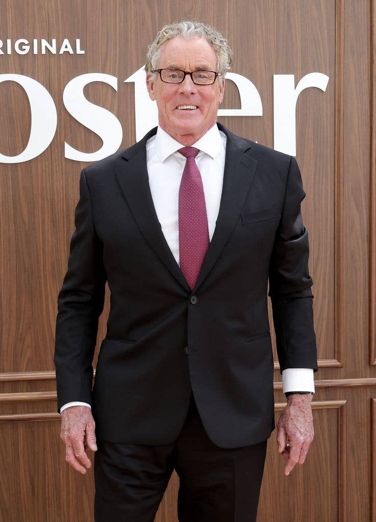 John C. McGinley in a black suit and red tie