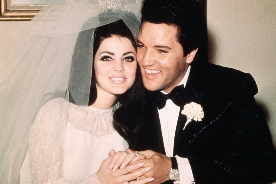 Elvis and Priscilla Presley smiling, dressed in wedding attire, holding hands.