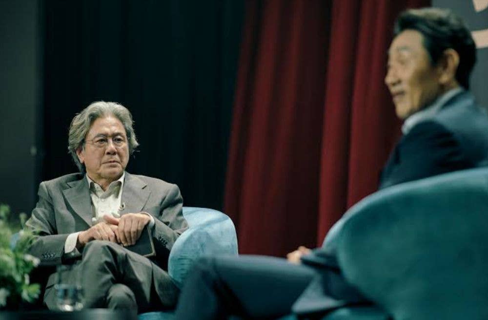 Heo Jun-ho and Choi Min-sik sit on blue chairs, engaged in conversation.