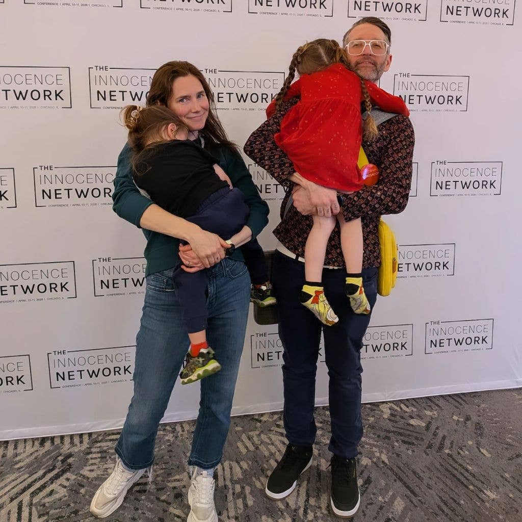 Amanda Knox and a man with glasses hold two children in front of an Innocence Network backdrop.