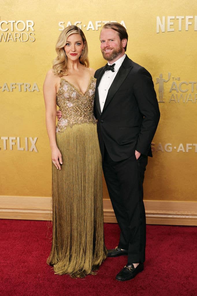 Abby Elliott and bill kennedy in formal wear pose on a red carpet at an awards event.