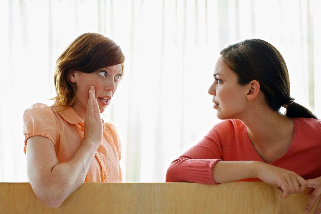 Two women in orange shirts sit at a desk, engaged in conversation.