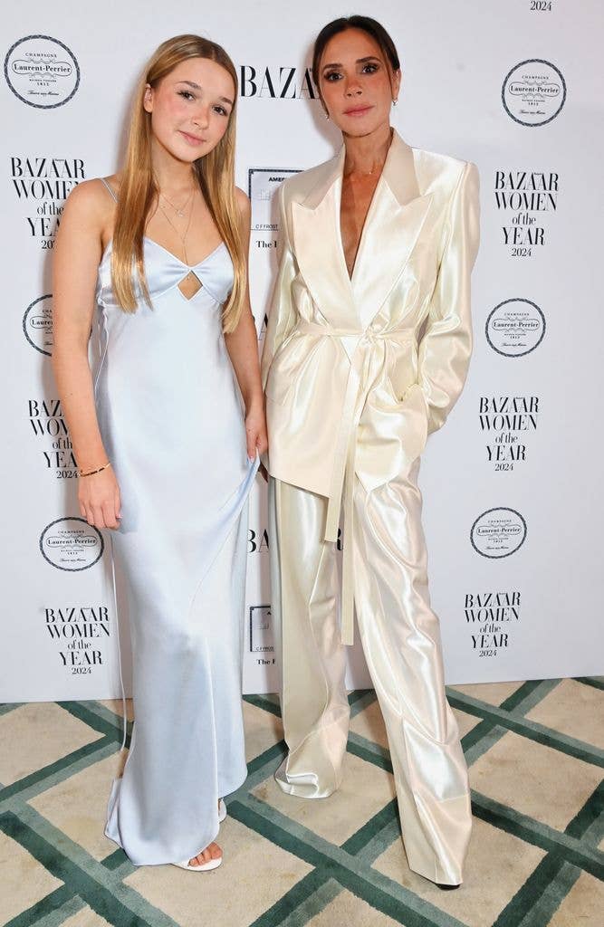Harper and Victoria Beckham pose on the red carpet, Harper wears a long white slip dress and Victoria a silky blazer and matching trousers