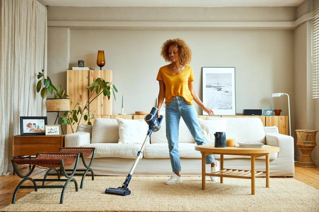 A woman in a yellow top and jeans is vacuuming a living room.
