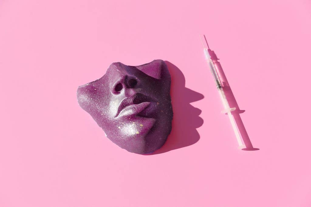 Purple face mask with glittery lips and eyes next to a syringe on pink background.
