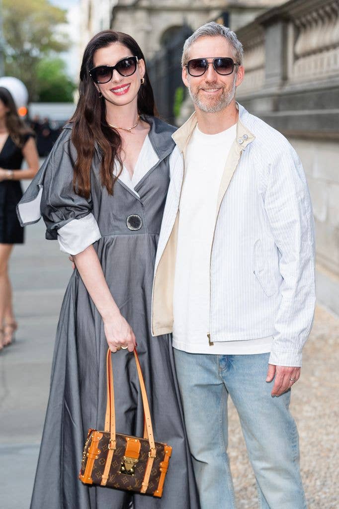 Anne Hathaway and Adam Shulman standing together, smiling, wearing sunglasses and casual clothing.