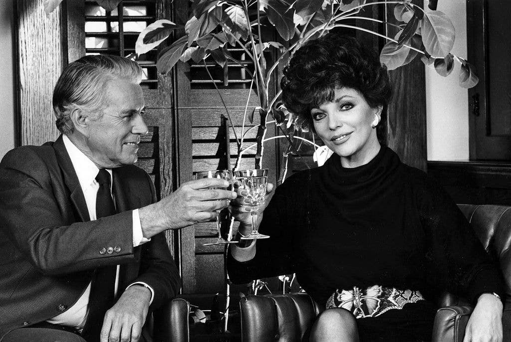 Actress Joan Collins (Alexis) and John Forsythe (Blake) share a toast in the boardroom of Producer Aaron Spelling during the 1985 season of the TV series Dynasty in Hollywood, California. (Photo by Eddie Sanderson/Getty Images).