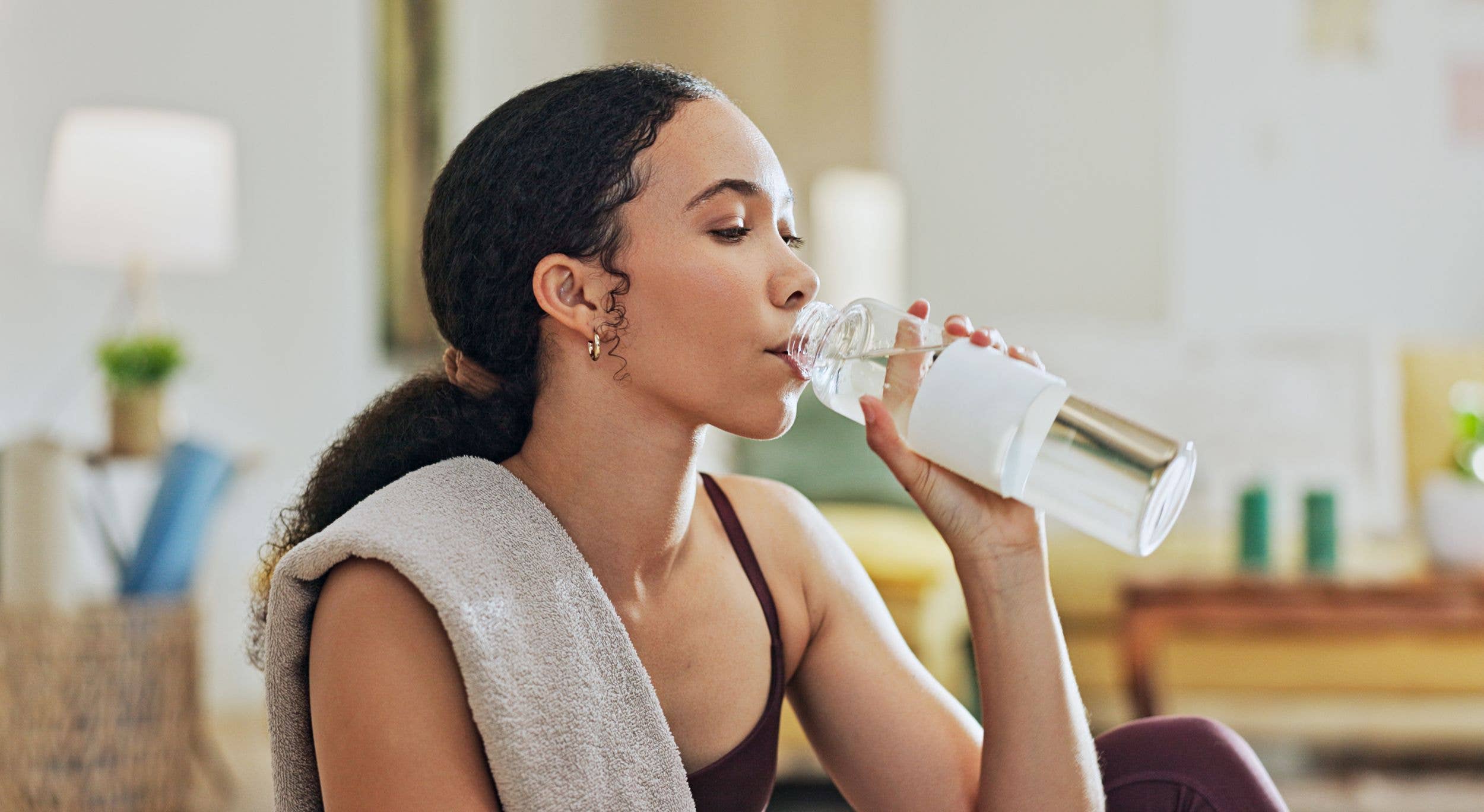 Woman, exercise and drinking water on floor in home with thinking, hydration or liquid for health detox. Girl, person and bottle for workout, nutrition and wellness with training for fitness in house