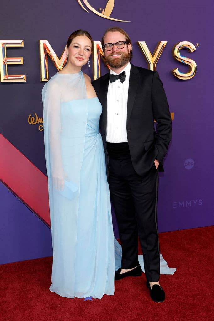 Abby Elliott in a blue gown and bill kennedy in a black tuxedo on a red carpet.