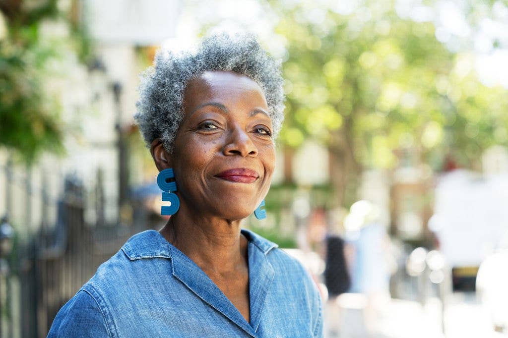 black woman with short grey natural hair, blue earrings and denim shirt looking confident