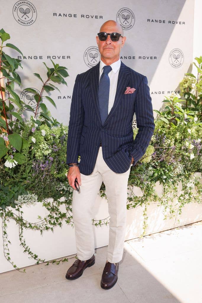 A photo of Stanley Tucci wearing a navy blue suit jacket and beige trousers 