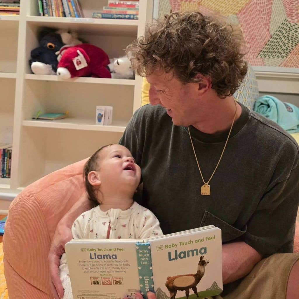 Mark Zuckerberg, with curly hair and a gold necklace, reads a book titled 'Llama' to a laughing baby.