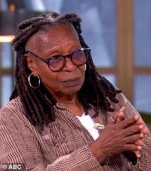 Whoopi Goldberg, wearing glasses and a plaid shirt, sits with hands clasped.