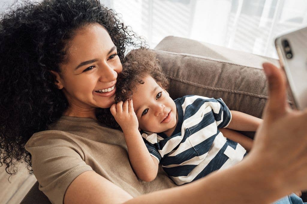 A woman with curly hair and a child in a striped shirt are taking a selfie.