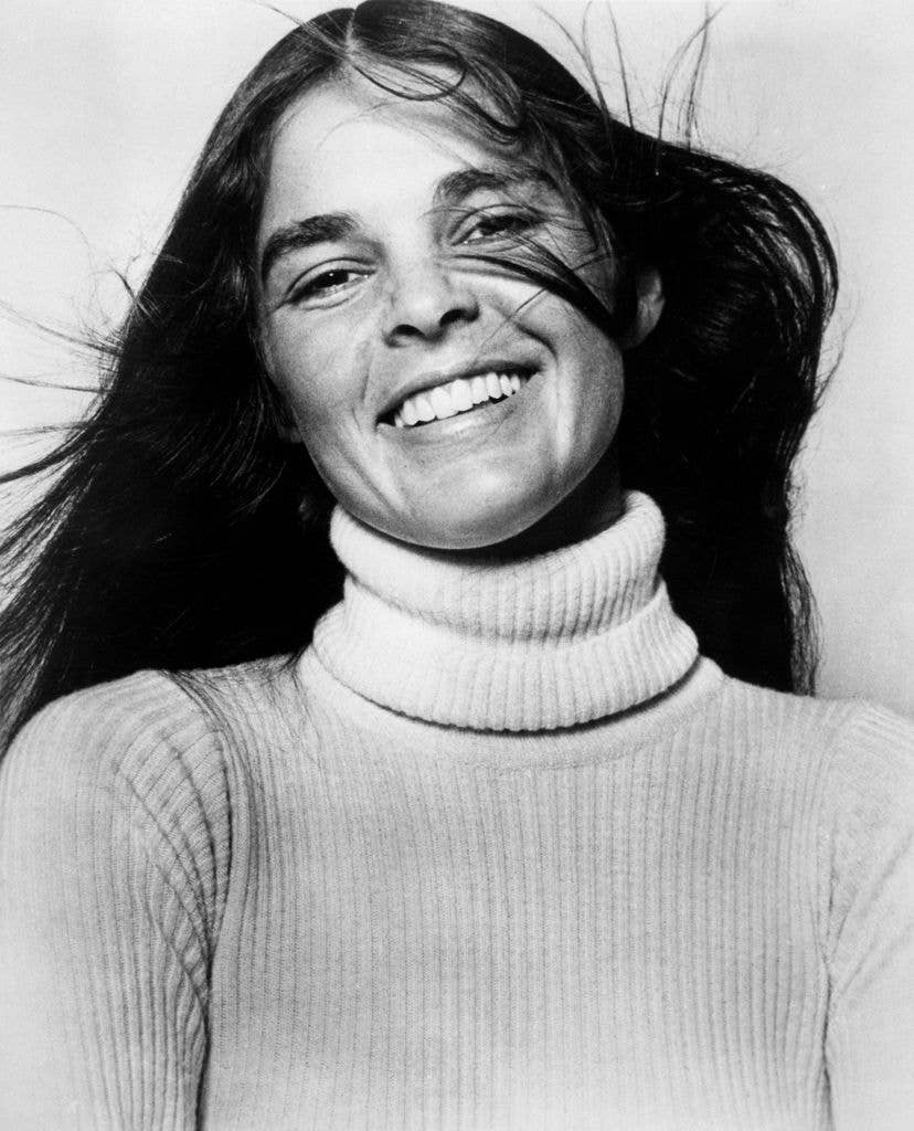 Headshot of Ali MacGraw smiling, wearing a turtleneck jumper in 1971.