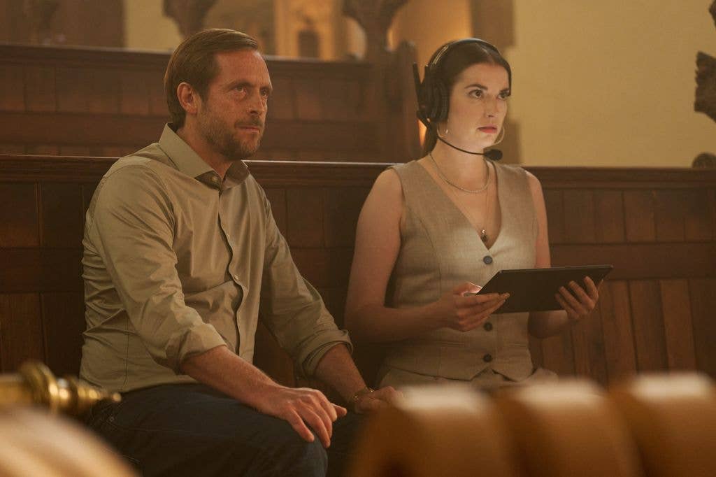 Stephen Campbell Moore sits next to a woman in a church, both wearing headsets.