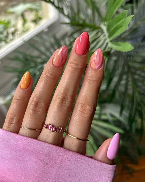 A person's hand with colorful nail polish and rings, set against a green plant background.