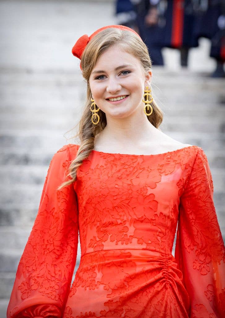 Princess Elisabeth in a red floral dress and gold earrings smiles on steps.