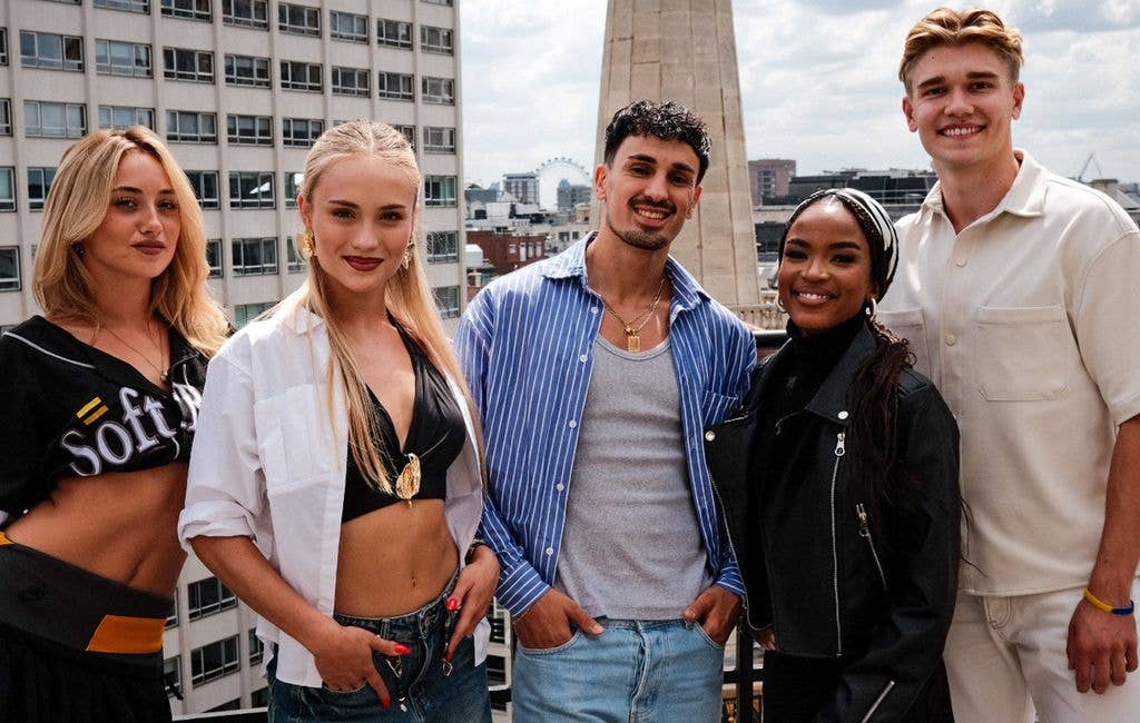 Five smiling individuals stand together on a rooftop, with a cityscape backdrop.