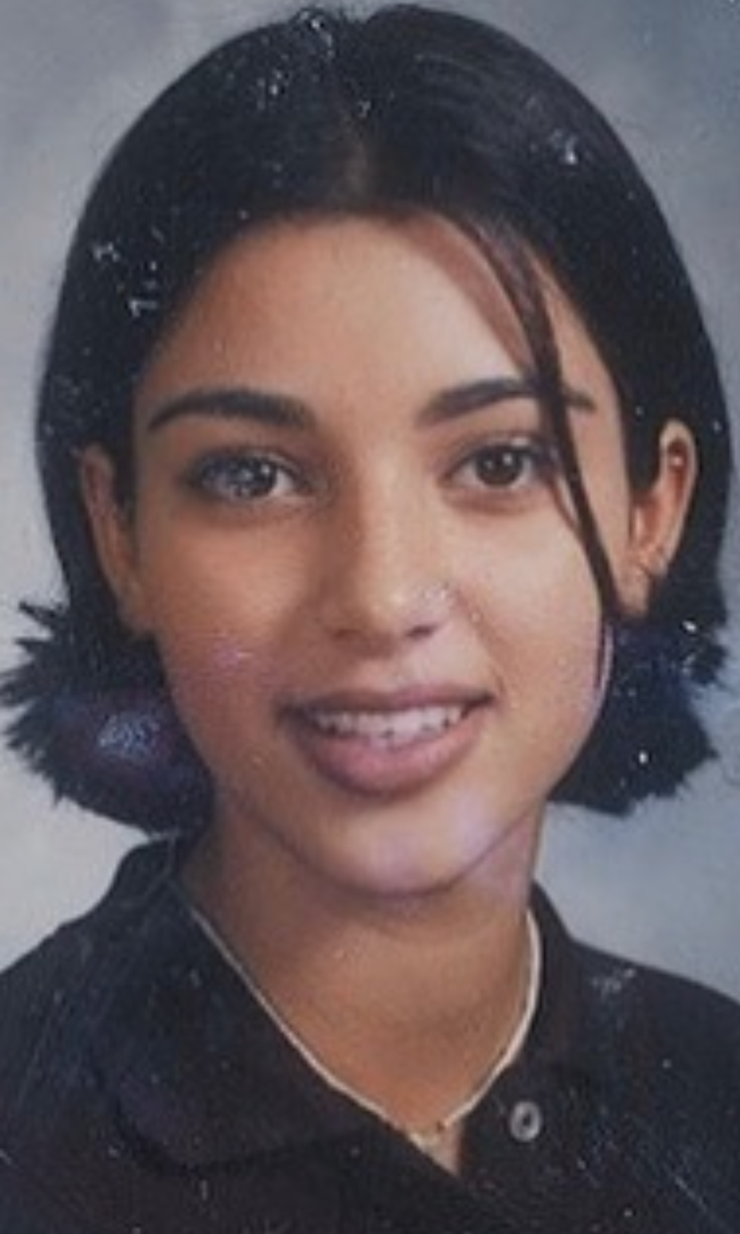 Portrait of a smiling woman with short black hair, wearing a black shirt and necklace.