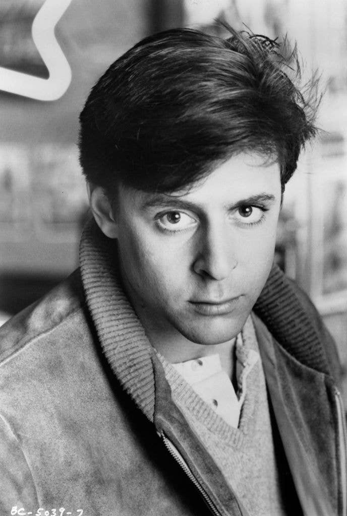 Judd Nelson in a black and white photo, wearing a jacket and sweater.