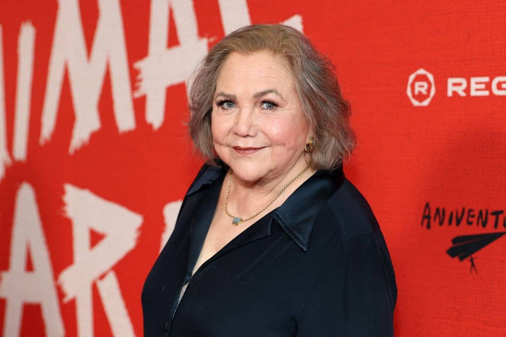 Kathleen Turner in a black top with collar looks sideways on to the camera.