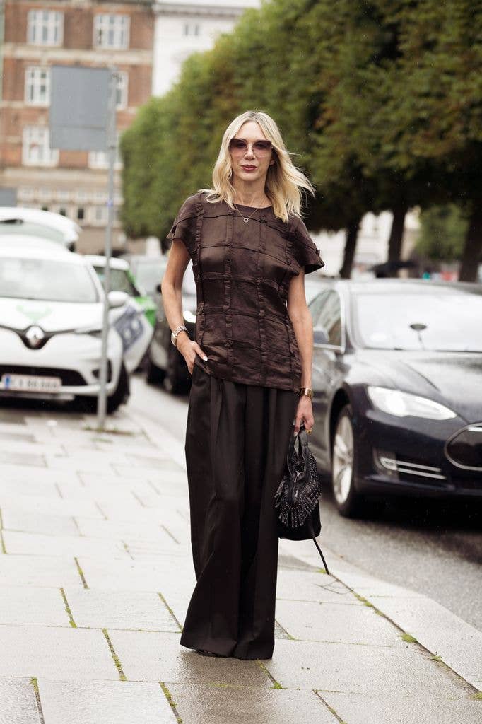 Melissa Vale wears wide brown pants, brown short sleeve top, ombre brown sunglasses, black bag with metal details outside MKDT show during the Copenhagen Fashion Week Spring/Summer 2027 on August 04, 2026 in Copenhagen, Denmark. (Photo by Raimonda Kulikauskiene/Getty Images)