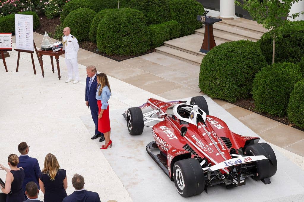 Melania and Donald pose in front of an IndyCar during an event announcing the expansion of a foster care initiative in the Rose Garden of the White House