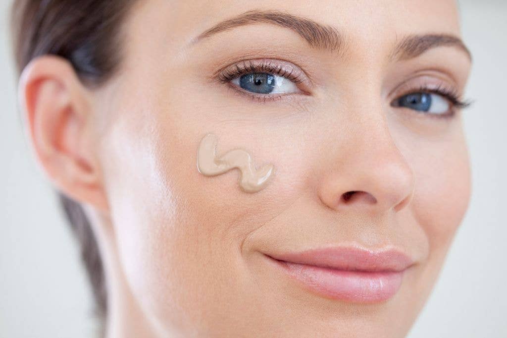 Close-up of a woman with blue eyes and short hair, applying cream to her cheek.