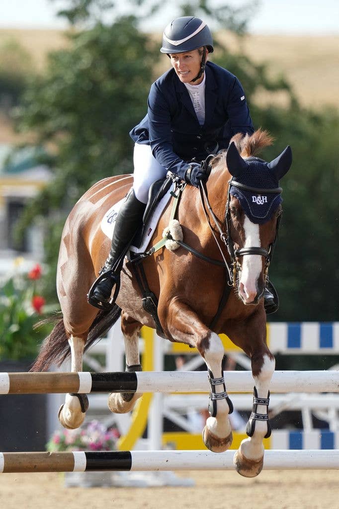 Zara Tindall riding a brown horse over a hurdle in a competition.